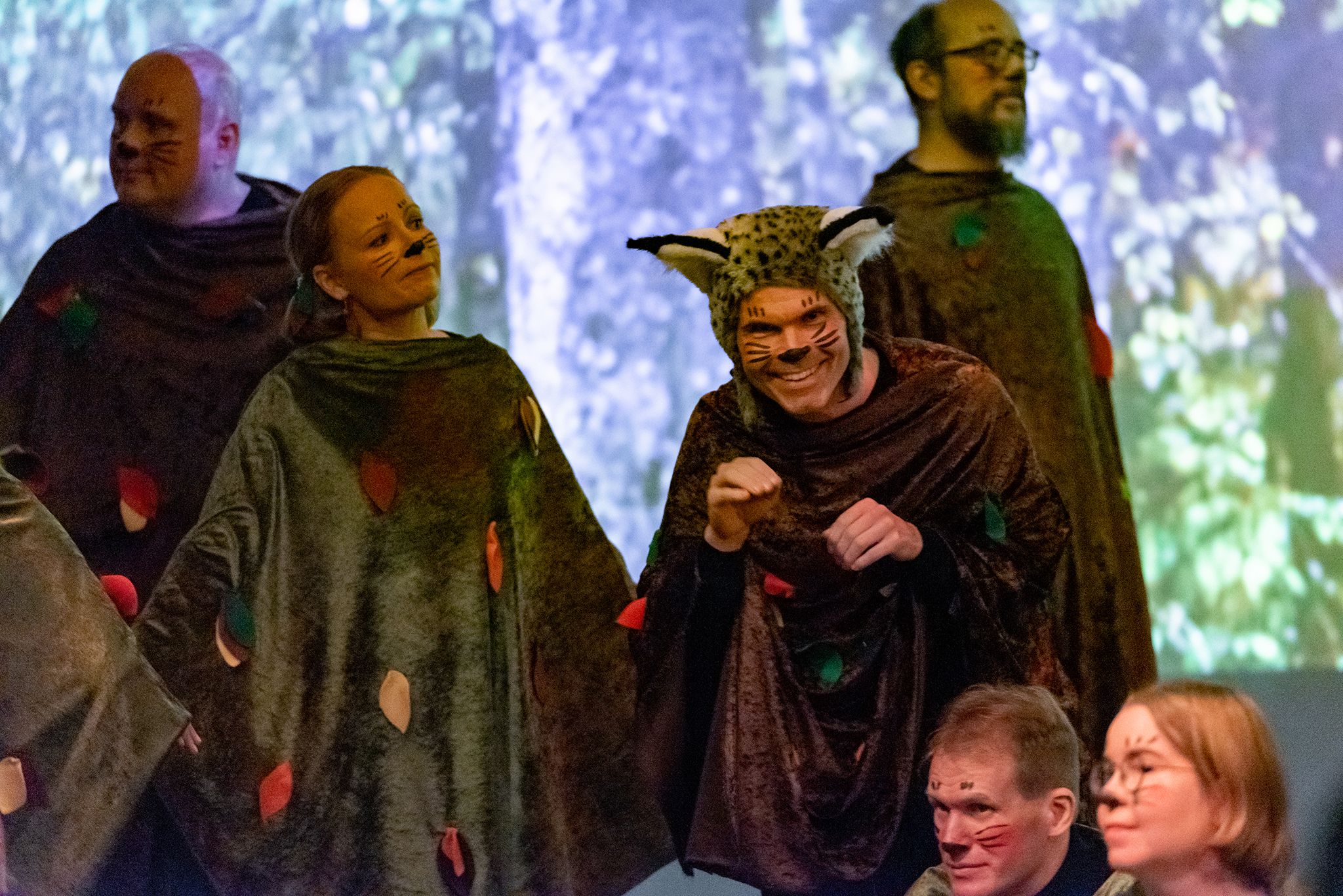 Kurolainen esittää hiipivää ilvestä ilvespäähine päässään muiden kuorolaisten keskellä lavalla