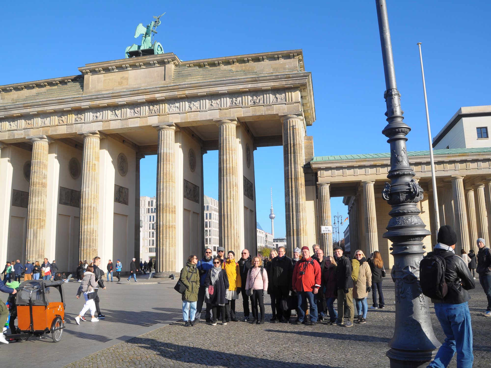 Kuorolaiset seisovat ryhmässä Brandenburgin portin edustalla aurinkoisena päivänä