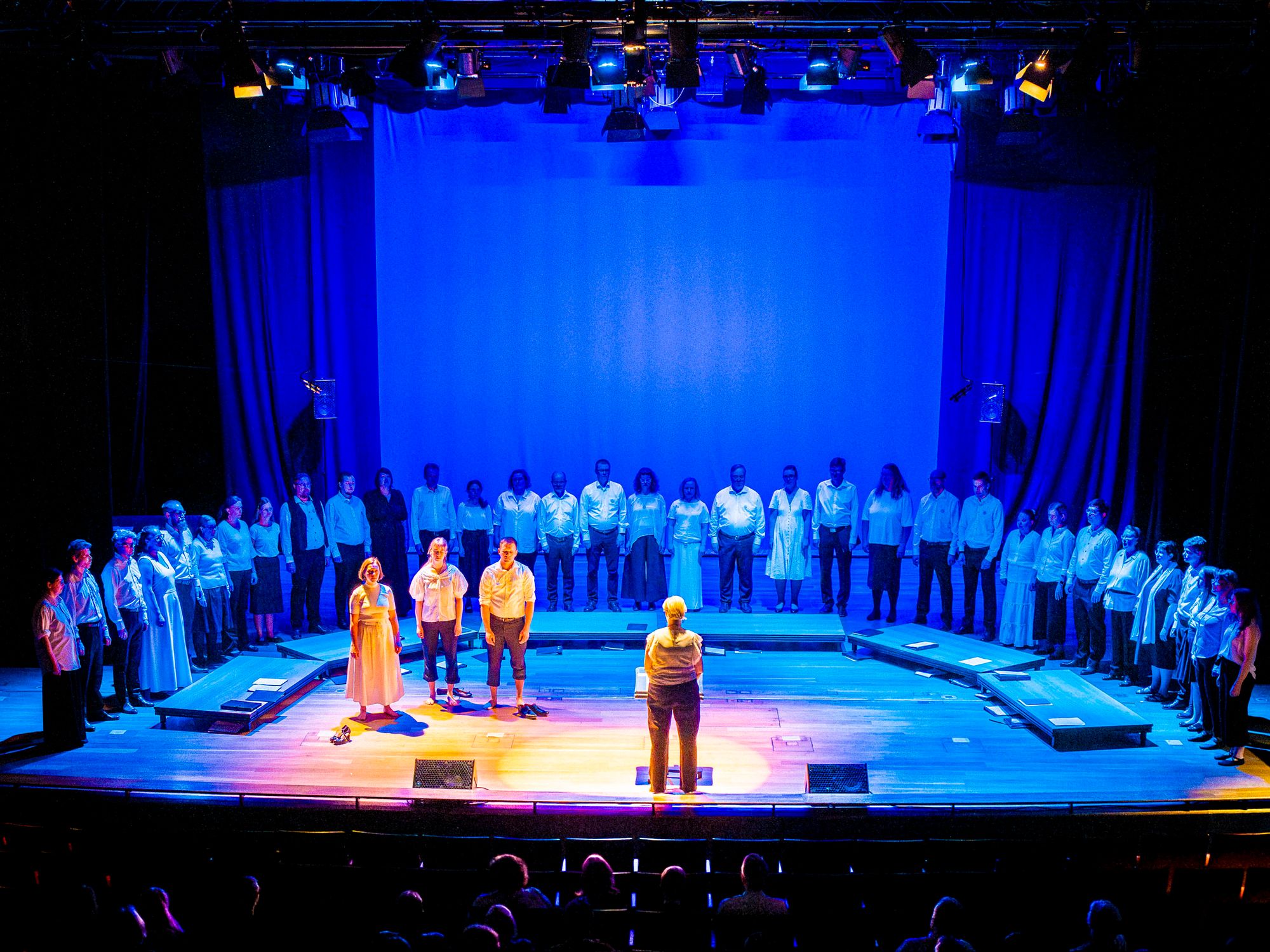 Kolme solistia keskellä kuoroa sinisessä valossa © Tuomas Tenkanen