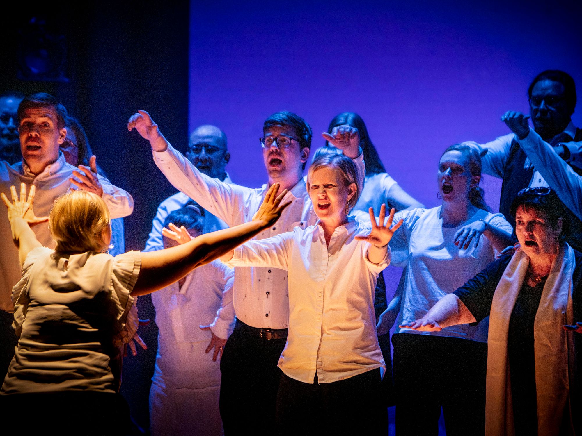 Kuorolaiset ojentavat kätensä dramaattisessa lavakohtauksessa © Tuomas Tenkanen