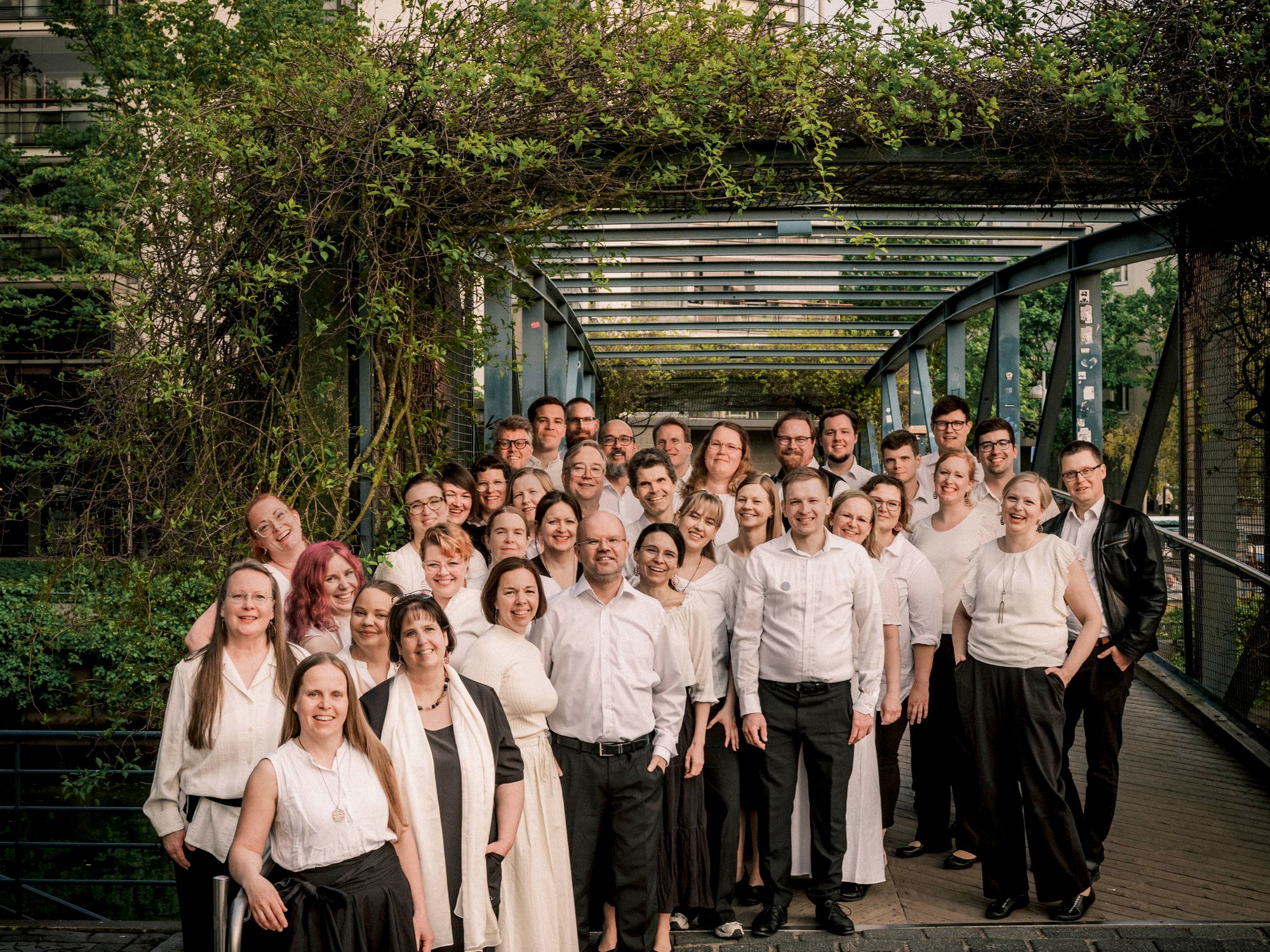 Kuorolaiset ryhmäkuvassa vehreällä kävelysillalla kaupungin keskellä © Tuomas Tenkanen