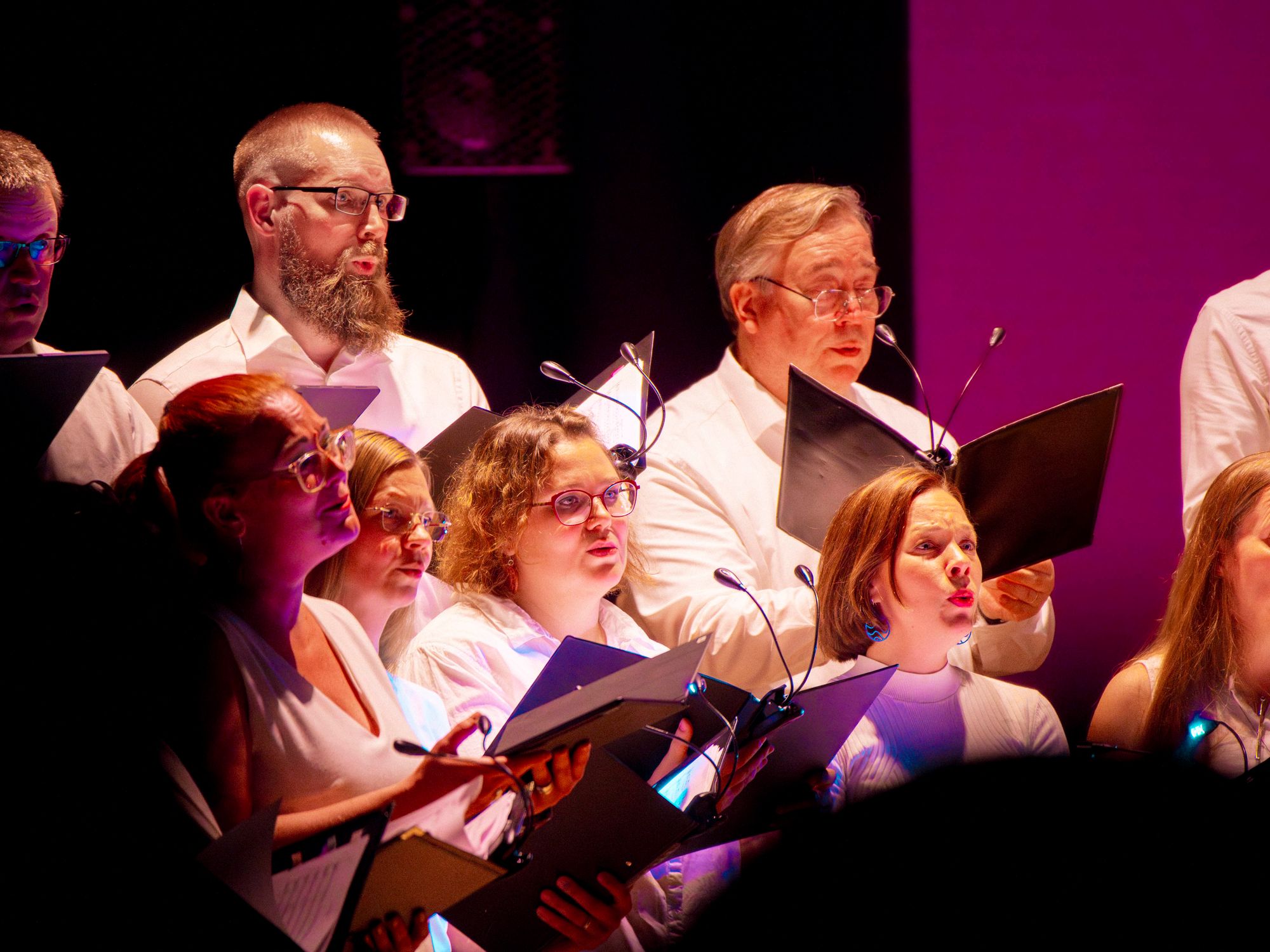Kuorolaisia valojen loisteessa laulaen keskittyneesti © Tuomas Tenkanen